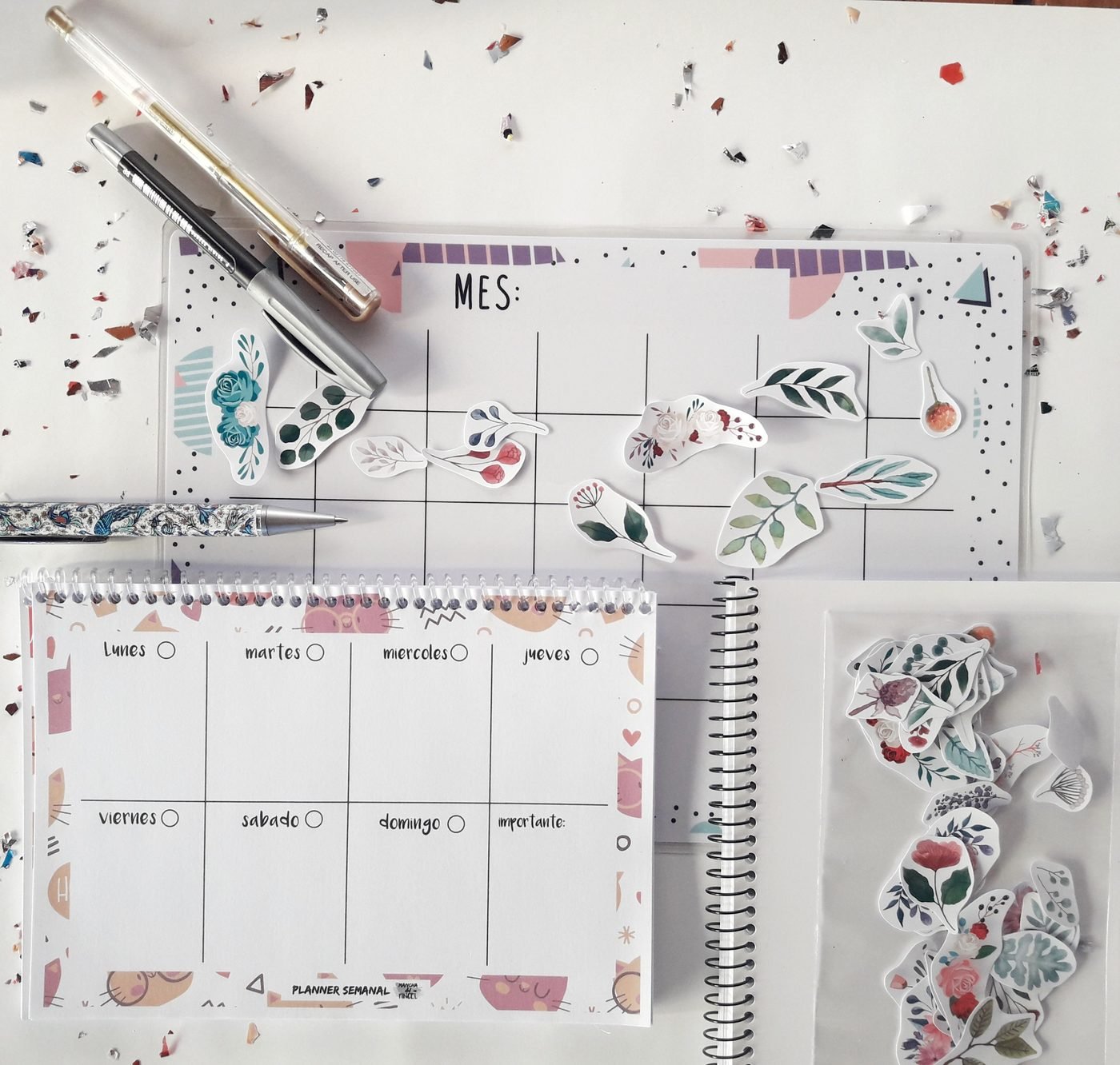Planificador mensual y semanal de papel sobre una mesa, con pegatinas y un rotulador.