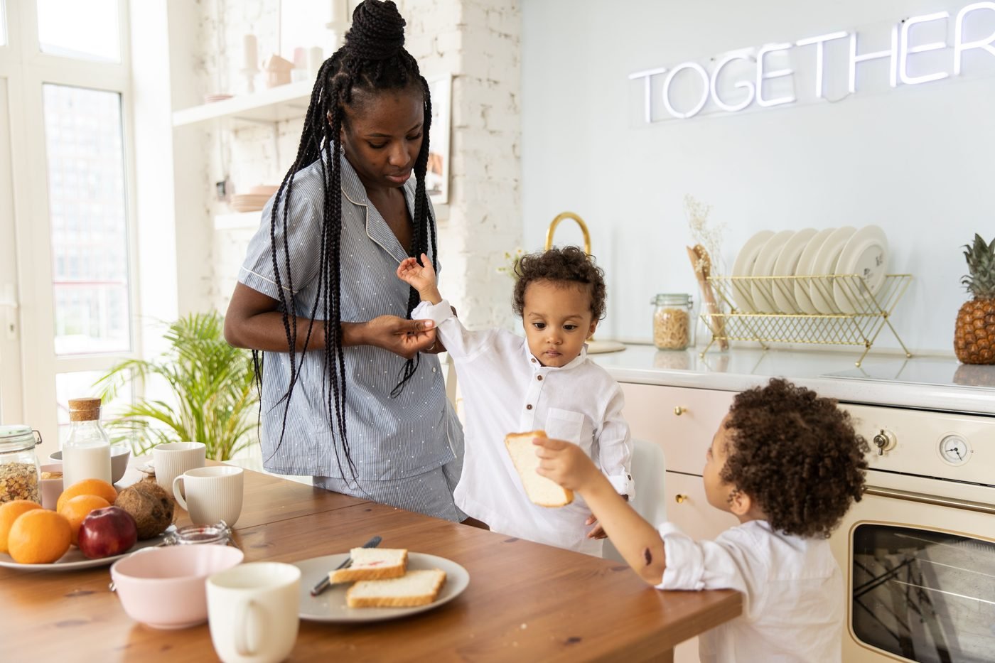 Madre y dos niños pequeños preparando juntos el desayuno en la cocina.