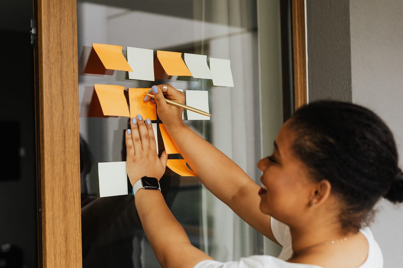 Mujer colocando notas adhesivas de colores sobre un panel de cristal.