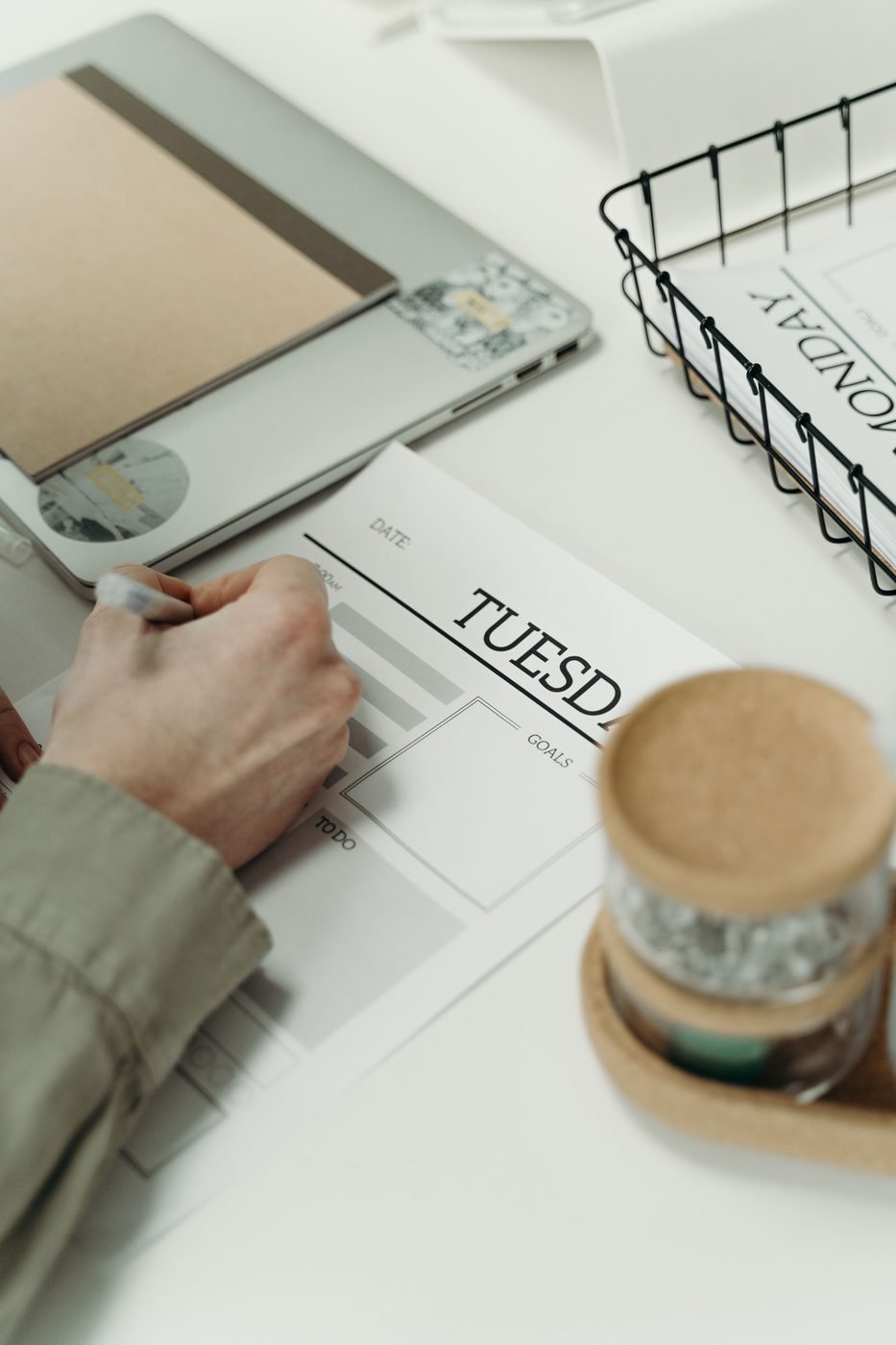 Mano escribiendo en un planificador semanal de papel sobre una mesa blanca.